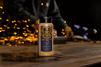 Tough Nut walnut shell hand cleaner bottle on a steel shop bench with grinder sparks behind