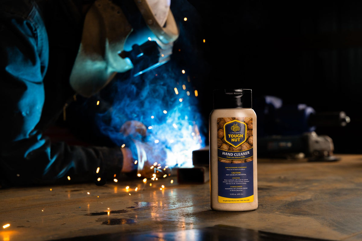 Tough Nut hand cleaner bottle on a welding table while a welder works behind it