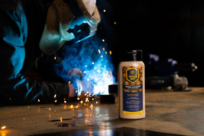 Tough Nut hand cleaner bottle on a welding table while a welder works behind it
