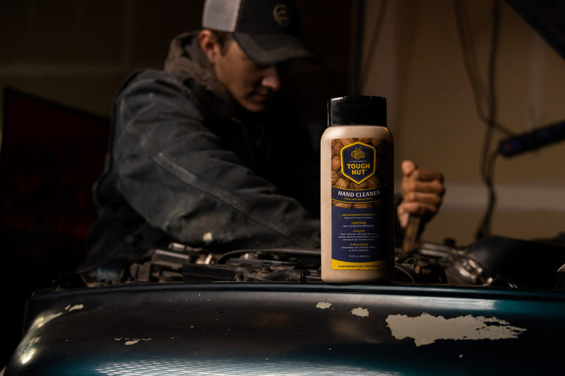 Tough Nut hand cleaner bottle on a truck hood while a mechanic works on the engine